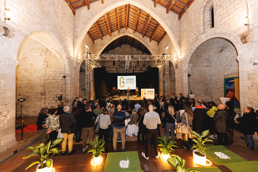 Panoràmica de l'espai de la festa amb els convidats d'esquena mirant l'escenari